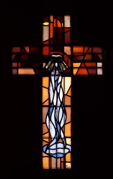 Verrière de la travée des fonts baptismaux reprensantant une croix où le corps du Christ est remplacé par une évocation de la fontaine de vie.