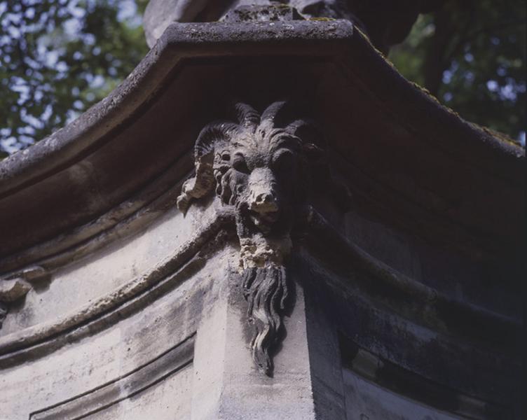 Fontaine en borne illustrant la gloire du roi Louis XV, autrefois sur le pont des Belles fontaines côté amont, replacée dans le parc du château de la Cour de France : tête de bélier supportant la corniche qui couronne le piédestal du groupe sculpté.