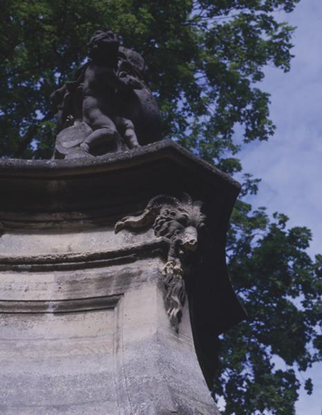 Fontaine en borne illustrant la gloire du roi Louis XV, autrefois sur le pont des Belles fontaines côté amont, replacée dans le parc du château de la Cour de France : tête de bélier supportant la corniche qui couronne le piédestal du groupe sculpté.
