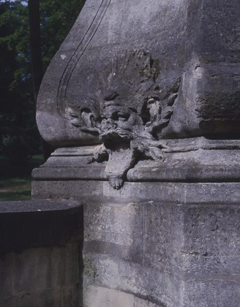 Fontaine en borne illustrant la gloire du roi Louis XV, autrefois sur le pont des Belles fontaines côté amont, replacée dans le parc du château de la Cour de France : mascaron ornant le piédestal du groupe sculpté et servant d'exutoire à l'eau de la fontaine recueillie dans la vasque..