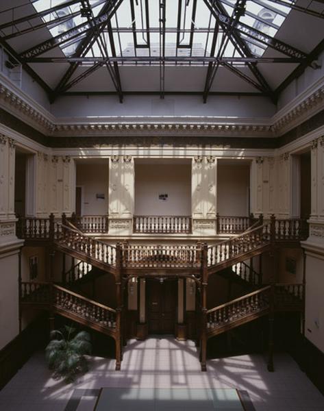 Le hall central : l'escalier en charpente, à double volée symétrique, conduisant à l'étage du hall.