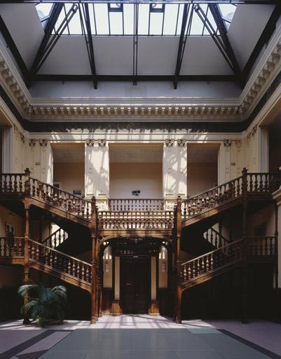 Le hall central : l'escalier en charpente, à double volée symétrique, conduisant à l'étage du hall.