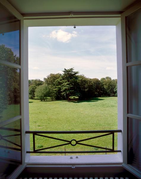 Parc du château : la pelouse et un groupe d'arbres dans l'encadrement d'une fenêtre du premier étage.