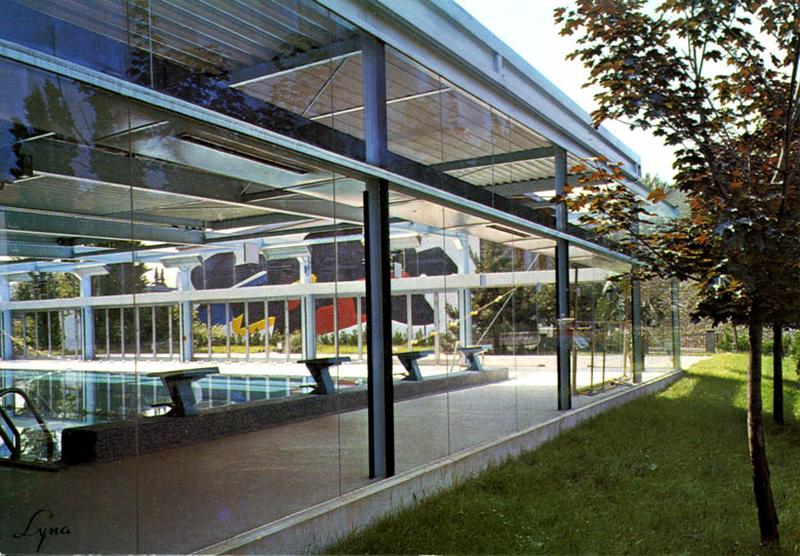 Vue latérale de la piscine avec une vue du pignon du gymnase en transparence.
