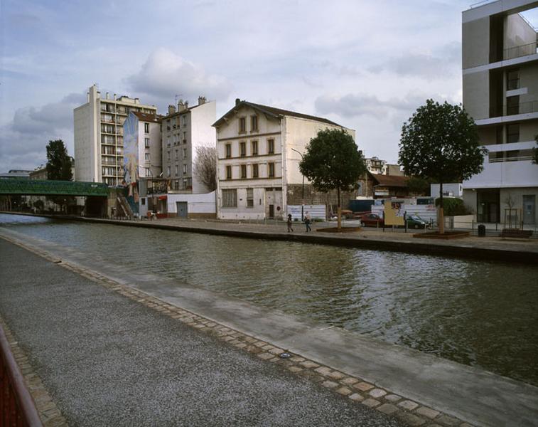 Vue de l'entrepôt industriel depuis la rive droite du Canal de l'Ourcq. A gauche, le pont Delizy.