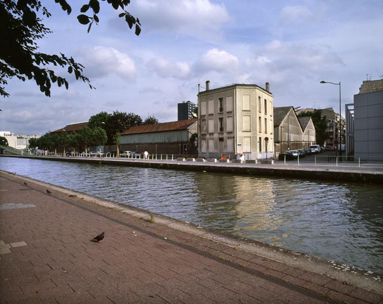 Vue du site industriel depuis la rive droite du canal. Au centre, immeuble d'habitation à l'angle de la rue Etienne Marcel et du quai de l'Aisne construit à la fin du 19e siècle, servant de logements aux employés des Comptoirs Français E. Mignot.