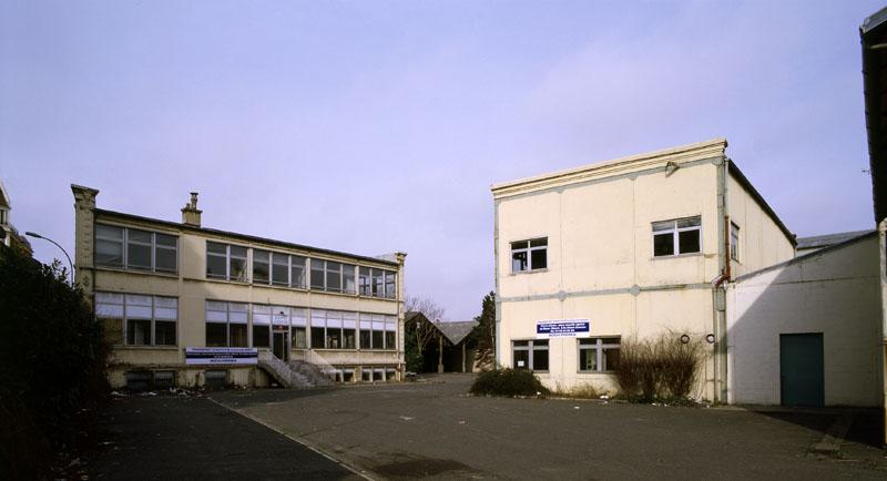 Vue du bâtiment administratif et de l'atelier de travail du bois depuis la cour du site industriel. A droite, petit appentis à l'emplacement duquel était situé le pont de graissage destiné à l'entretien des véhicules automobiles des Comptoirs Français E. Mignot.