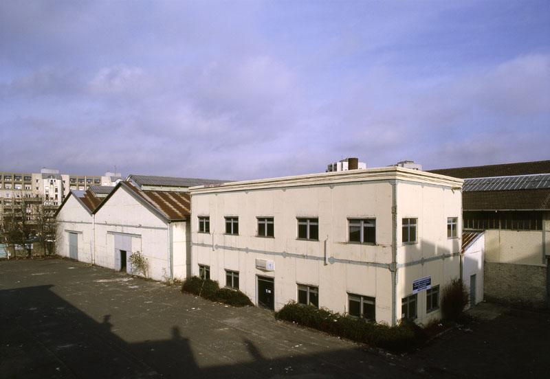 Vue de l'atelier de travail du bois et des entrepôts à toiture à longs pans depuis le 1er étage du bâtiment administratif.