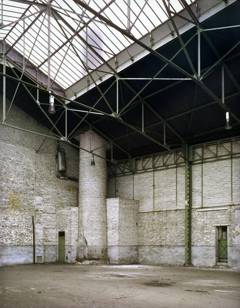 Vue intérieure des entrepôts à toiture à longs pans situés le long du quai de l'Aisne. Au second plan, la base de la cheminée en briques du site industriel.