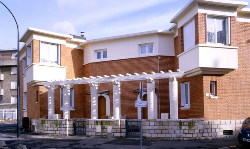 Maisons jumelles reliées par une pergola en béton.