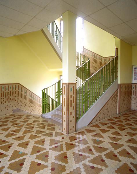 Intérieur d'une cage d'escalier du groupe scolaire Albert-Thomas. Le sol et une partie des murs sont revêtus d'un carrelage assemblé en motifs géométriques.