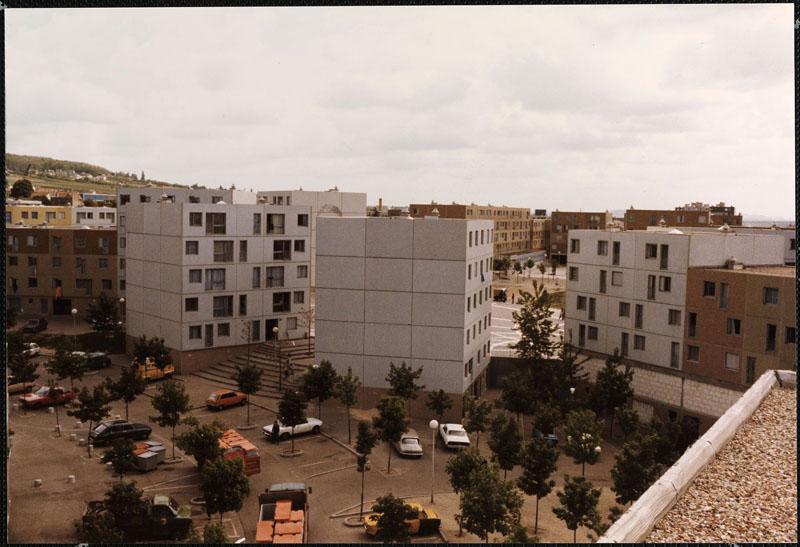 Vue du revers de la place de la Coquille. On peut voir trois des six petits bâtiments plot (comprenant un mur pignon aveugle donnant sur la place et couvert chacun d'un portrait de poète français du XIXe siècle). A gauche, le bâtiment de Victor Hugo (aujourd'hui détruit) ; au centre le bâtiment de Baudelaire, à droite le bâtiment de Rimbaud. Au delà, on entre-aperçoit la place du Pas qui n'aurait pas du être visible si l'hôtel de ville prévu pour refermer la place de la Coquille avait été construit.