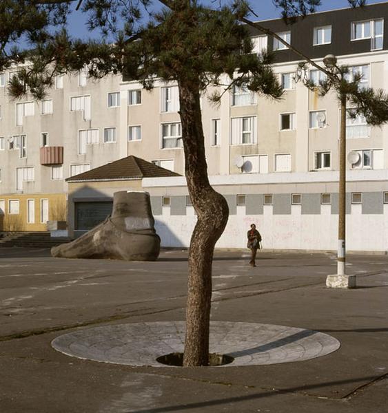 Détail de la partie haute de la place du Pas. La trame au sol formant le motif de dallage a presque disparu. Le seul décor sur la place, à l'exception du pied, est le pin, au premier plan, choisi par Aillaud pour son tronc tordu. Il sort d'un disque creux de marbre blanc.