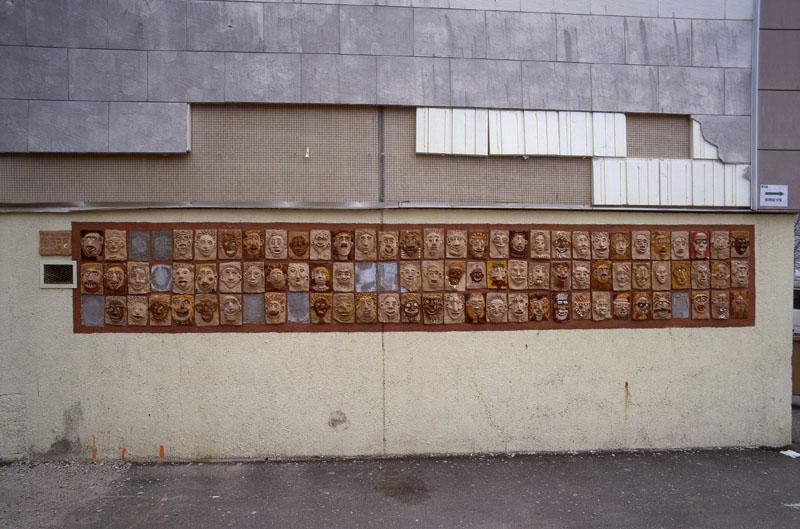 Détail actuel d'un mur pignon de la place des Arcades comportant un bas relief fait de 69 pièces représentant des visages. Oeuvre intitulée ' mur des sourires ' ' réalisé par des enfants et des adultes à Chantecolor avec Daniel. 2004/2005 '.