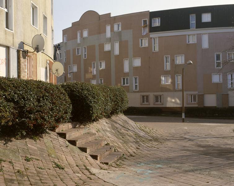 Vue actuelle de la place des Quatre-Vents. Détail du traitement du sol de briques remontant vers les bâtiments. Des marches dans les talus donnent accès aux immeubles.