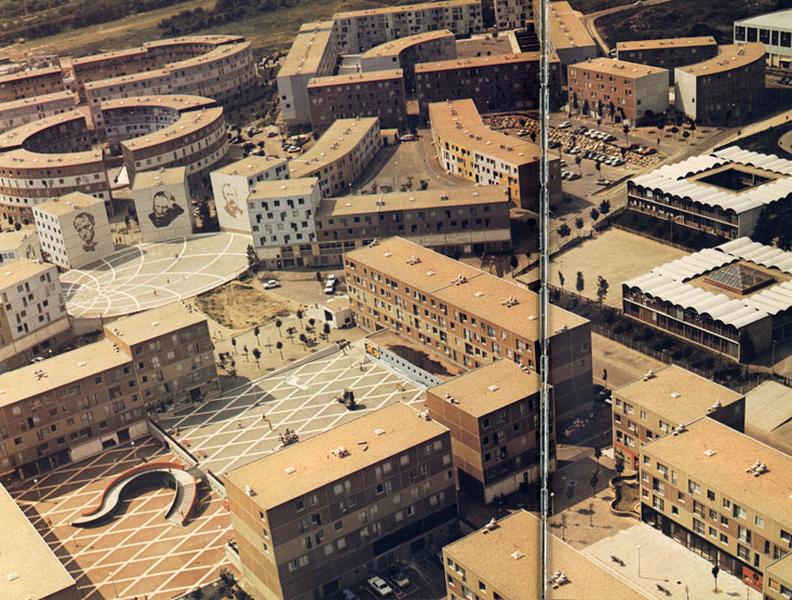 Vue aérienne. Au premier plan, la place du Pas ; en bas à doite la place des Pierreuses ; au second plan de gauche à droite : la place de la Coquille (avec les murs pignon des poètes), la place du Trident et l'école primaire R. Dorgelès. Au troisième plan, de gauche à droite, les places de la Lance et de l'Hippodrome, la place de l'Eté-Vert et la place de l'Ysé. Les trames au sol des places de la Coquille et du Pas sont bien visibles. Sur cette dernière, au devant de la sculpture du pied, la trace blanche laissée par le pas est également bien visible (aujourd'hui détruite).