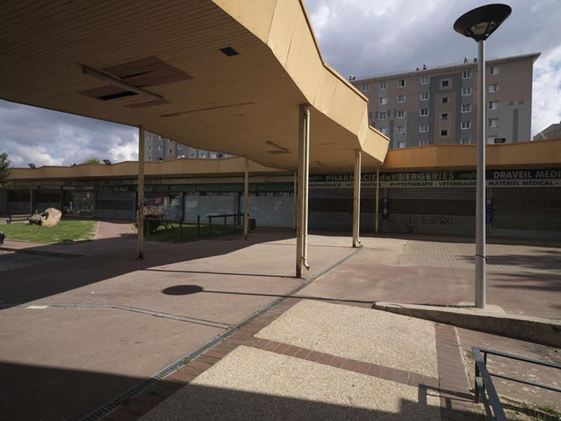 La cité des Bergeries à Draveil : la galerie sous auvent du centre commercial, reliant le bar-tabac à la galerie marchande en rez-de-chaussée, dont une partie se trouve sur la commune de Vigneux (ainsi que l'immeuble barre à l'arrière-plan).