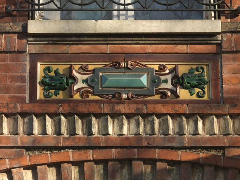Bas-relief en cartouche composé de carreaux de faïence émaillée, surmontant les fenêtres du rez-de-chaussée.