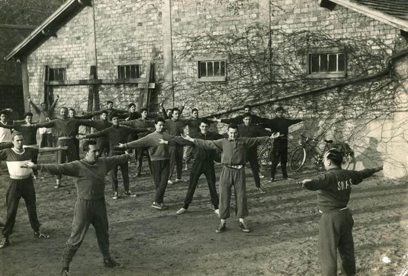 Membres du club en train de faire des mouvements de gymnastique à côté du hangar.