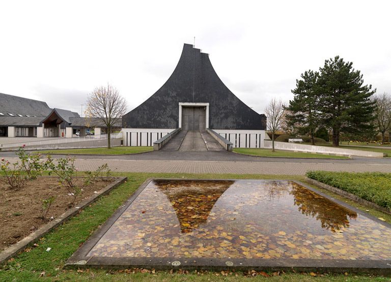 Dans l'axe, le bâtiment des cérémonies et sa rampe d'accès (symétrique à celle de l'extérieur du cimetière) se reflétant dans un des miroirs d'eau de la composition de Székely.