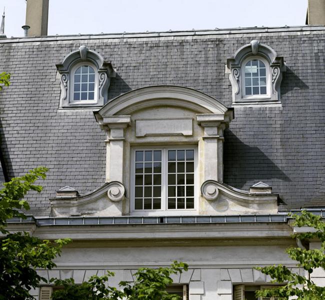 Détail de la lucarne centrale sur la façade antérieure : accostée par deux volutes, encadrée de pilastre et sommé d'un fronton cintré. On peut encore deviner sur la table soulignant le linteau l'inscription ste Anne, nom de l'orphelinat qui a occupé les lieux.