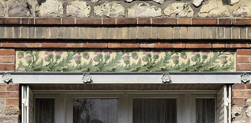 Détail de la frise de céramique ornant le dessus du linteau métallique de la baie du rez-de-chaussée. Motif végétal : fleurs de chardon.