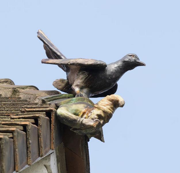 Détail de l'un des ornements de faîtage (about de rive) du toit de la maison (façade sur rue) en céramique vernissée. Motifs animal et humain : pigeon posé sur un nain en buste.