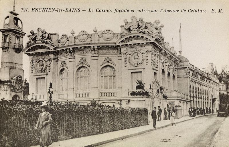 Nouveau casino de 1909 : vue perspective depuis l'avenue de Ceinture. La façade du théâtre est l'une des plus imposantes de l'ensemble du casino. Manifeste de l'art 1900, elle est caractéristique par l'exubérance de la sculpture dans les parties hautes. Des personnages féminins surdimensionnés installés sur les frontons cintrés situés aux angles encadrent des lyres et semblent contempler le public, le visage penchée vers le bas. Un cumul de mascarons, guirlandes et pots à feu complètent ce décor.