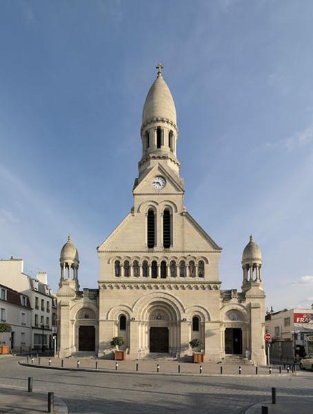 Vue d'ensemble de la façade occidentale. Au centre, au milieu de la frise de saints disposés dans des arcades, sont disposées deux baies ornées de verrières représentant un ostensoir et un ciboire. Il est à noter que cette représentation de l'eucharistie et de l'ostie sur une façade de cette période est un phénomène assez rare.