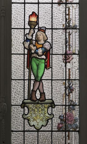 Détail de l'un des deux personnages, porte-torchère, néo-Renaissance, ornant l'un des panneaux supérieurs des baies du bow-window. L'ensemble de la composition est bordé d'une frise de roses sur une tige rectiligne et épineuse.