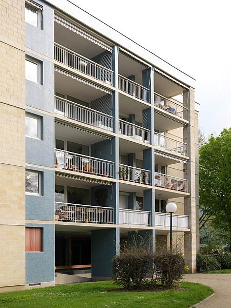 Façade principale du bâtiment 3 en L situé côté parc de la Blanchette. Ce corps de bâtiment constitue la retour du L marqué par le décrochement au niveau du balcon de droite. La façade est rythmée verticalement par les refends porteurs qui se prolongent horizontalement sur les balcons et verticalement pour jouer le rôle de pilotis. L'alternance de la pierre de Saint-Maximin et de la mosaïque bleue rythme la façade.