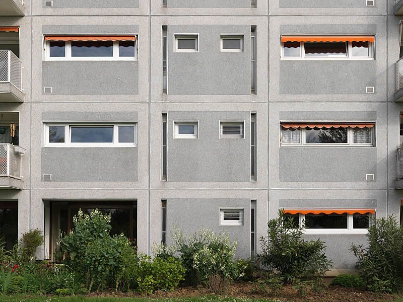 Détail d'une façade : combinaison de deux types de panneaux préfabriqués avec des stores d'origine à certaines fenêtres.