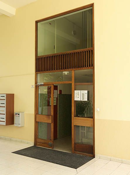 Détail d'une porte donnant accès aux escaliers et à l'ascenseur d'une barre R+10. Les huisseries en bois sont d'origine, de même que les boîtes aux lettres. La cage d'escaliers est recouverte en partie basse d'un décor en céramique verte.