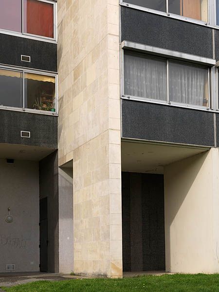 Alternance de parpaings de pierre et demosaïque de grès cérame gris.Ce détail du plan de construction de la tour : les panneaux de cuisine sont décrochés des panneaux des séjours et chambres, il s'agit d'une construction selon un plan écartelé et décalé du noyau central. Ce décrochement laisse apparaître le refend porteur en pierre perpendiculaire à la façade.