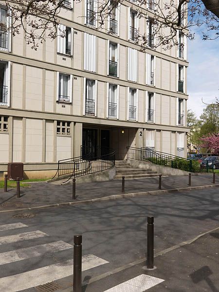 Entrée d'immeuble avec un escalier à volée droite dans l'alignement et double rampe d'accès en volute sur les côtés.