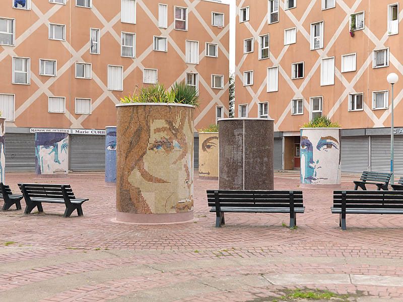 Place aux herbes avec bacs à fleurs décorés de mosaïques représentant des visages. Vue rapprochée.