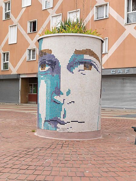 Place aux herbes, bac à fleurs avec décor d'un visage en mosaïque.