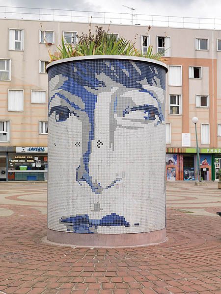 Place aux herbes, bac à fleurs avec décor d'un visage en mosaïque.