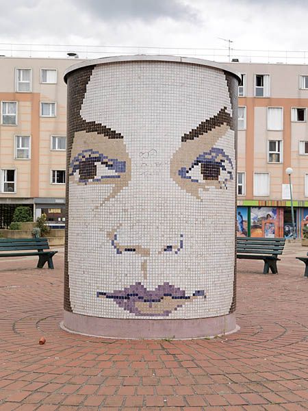 Place aux herbes, bac à fleurs avec décor d'un visage en mosaïque.