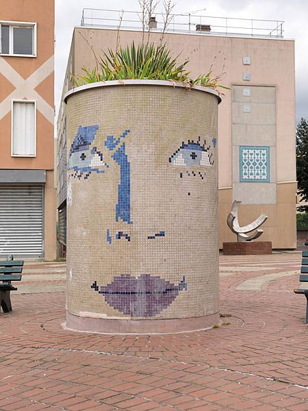 Place aux herbes, bac à fleurs avec décor d'un visage en mosaïque.