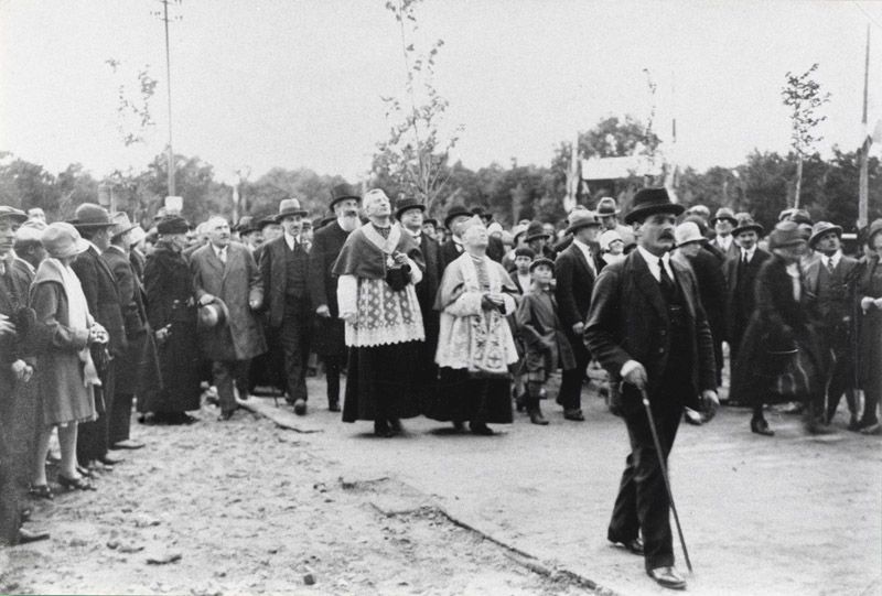 Cérémonie d'inauguration de l'église en présence du Curé commanditaire et des personnalités d'Elisabethville qui contemplent la façade. Photographie, 1929. (AM Aubergenville).