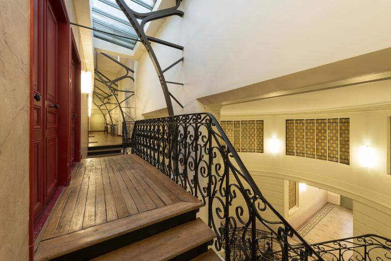 Vue depuis le haut du grand escalier sur le couloir menant aux ateliers et sur ses rampes en ferronerie (bâtiment côté cour et rue Ganneron)