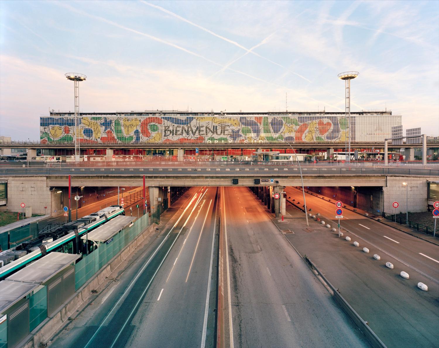 2018, Orly-Sud, la station Aéroport d'Orly du tramway T7 et la Nationale 7, la façade de l'aérogare est décorée d' "Orlove" une œuvre de Jean-Charles de Castelbajac, vue prise depuis le nord. 