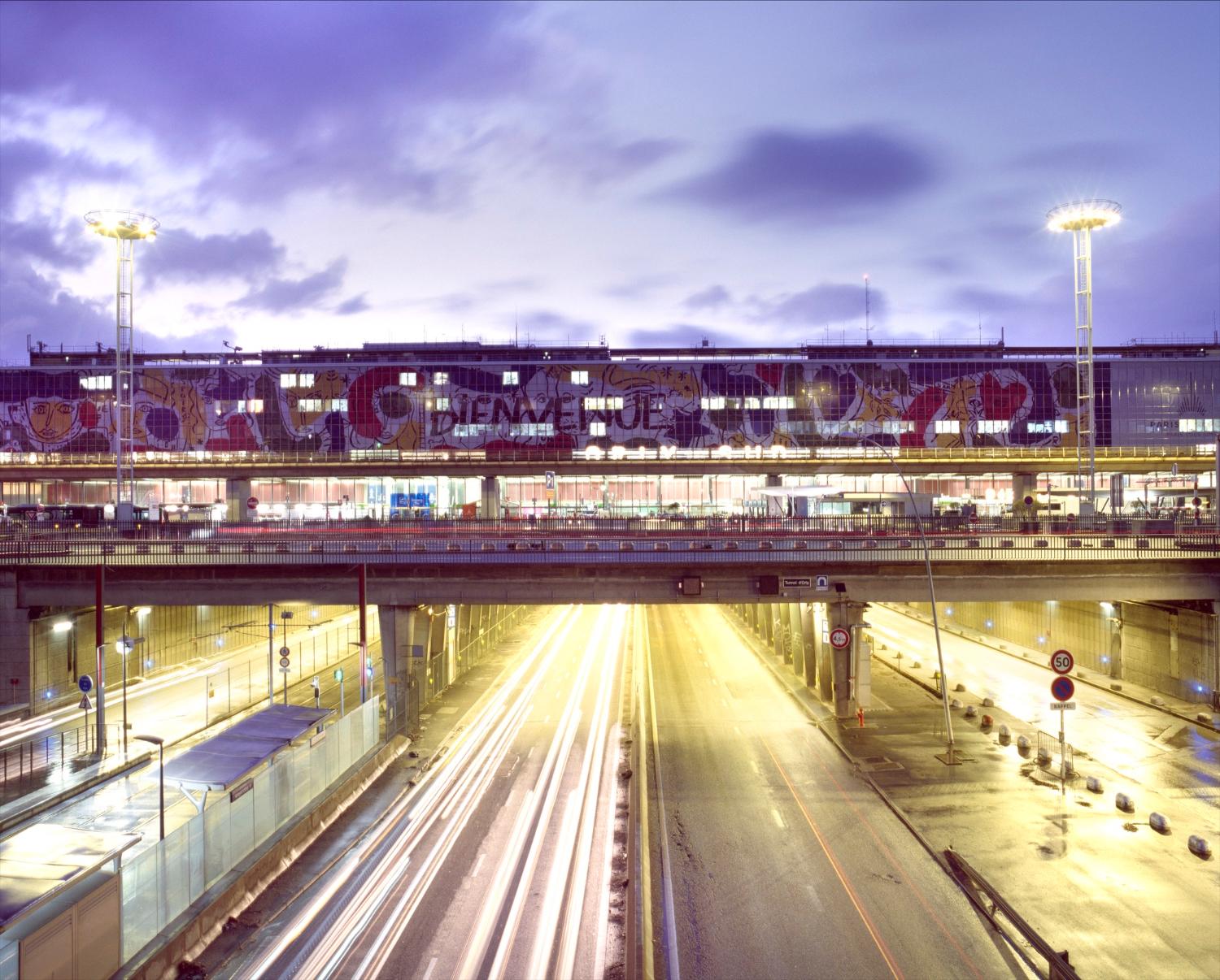 2018, Orly-Sud, la station Aéroport d'Orly du tramway T7 et la Nationale 7, la façade de l'aérogare est décorée d' "Orlove" une œuvre de Jean-Charles de Castelbajac, vue prise depuis le nord. 