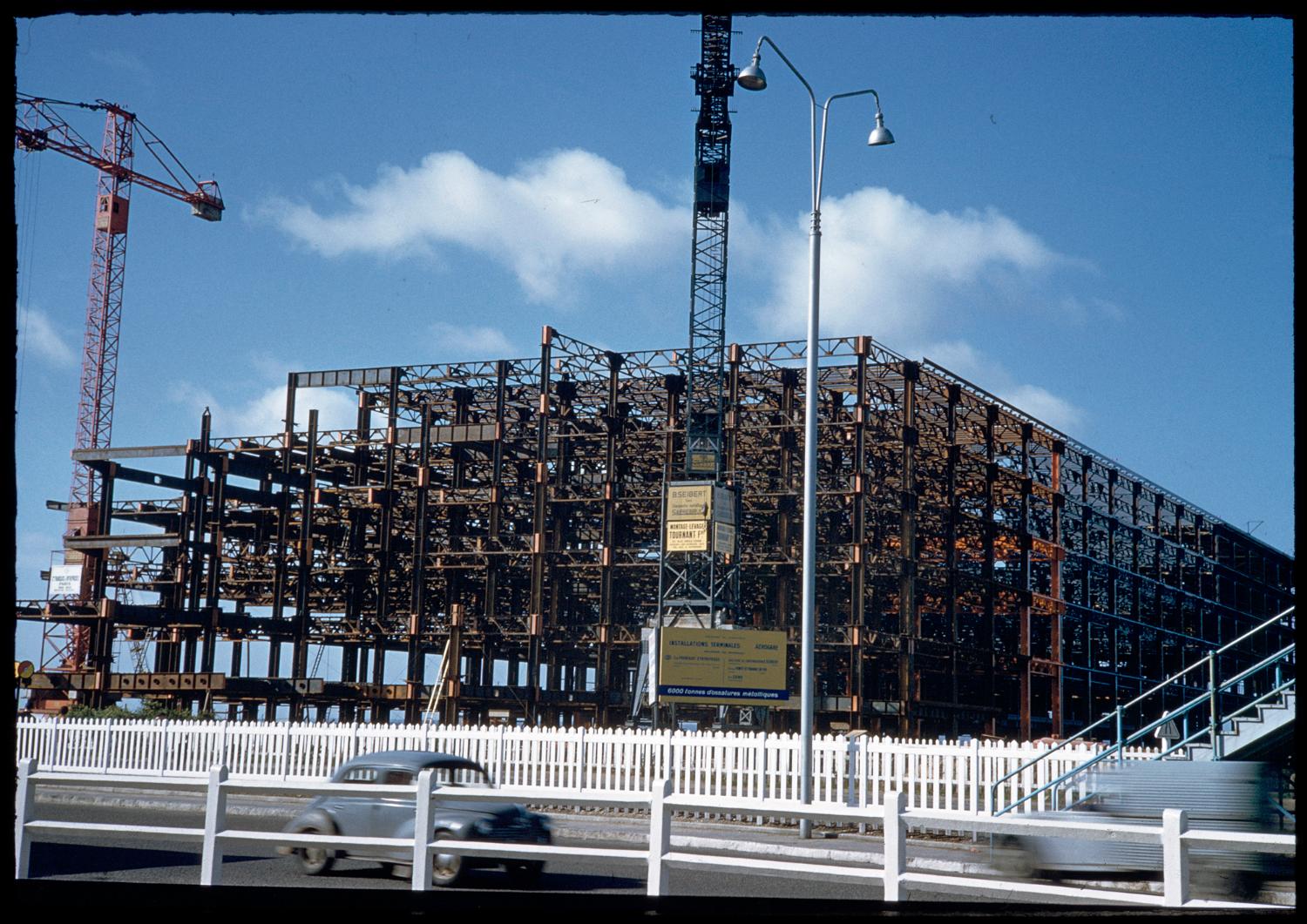 1957 1961, la construction des Installations Terminales, le montage de l'ossature métallique en 1958, on distingue les voitures sur la nationale 7 (ancien tracé) au premier plan, vue prise depuis le nord est.