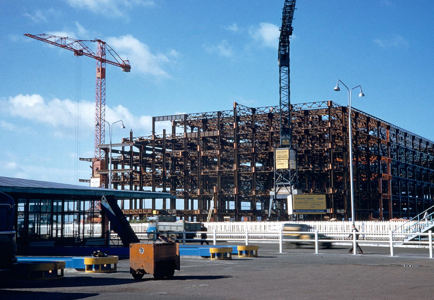 1957 1961, la construction des Installations Terminales, le montage de l'ossature métallique en 1958, on distingue les voitures sur la nationale 7 (ancien tracé) au premier plan, vue prise depuis l'est (Aérogare-Sud).