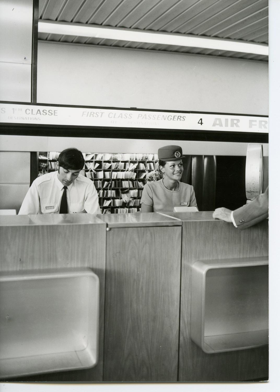 Rez-de-chaussée, comptoir d'accueil des passagers de 1ère classe d'Air France, hôtesse en uniforme d'été de Cristobal Balenciaga de 1970. 