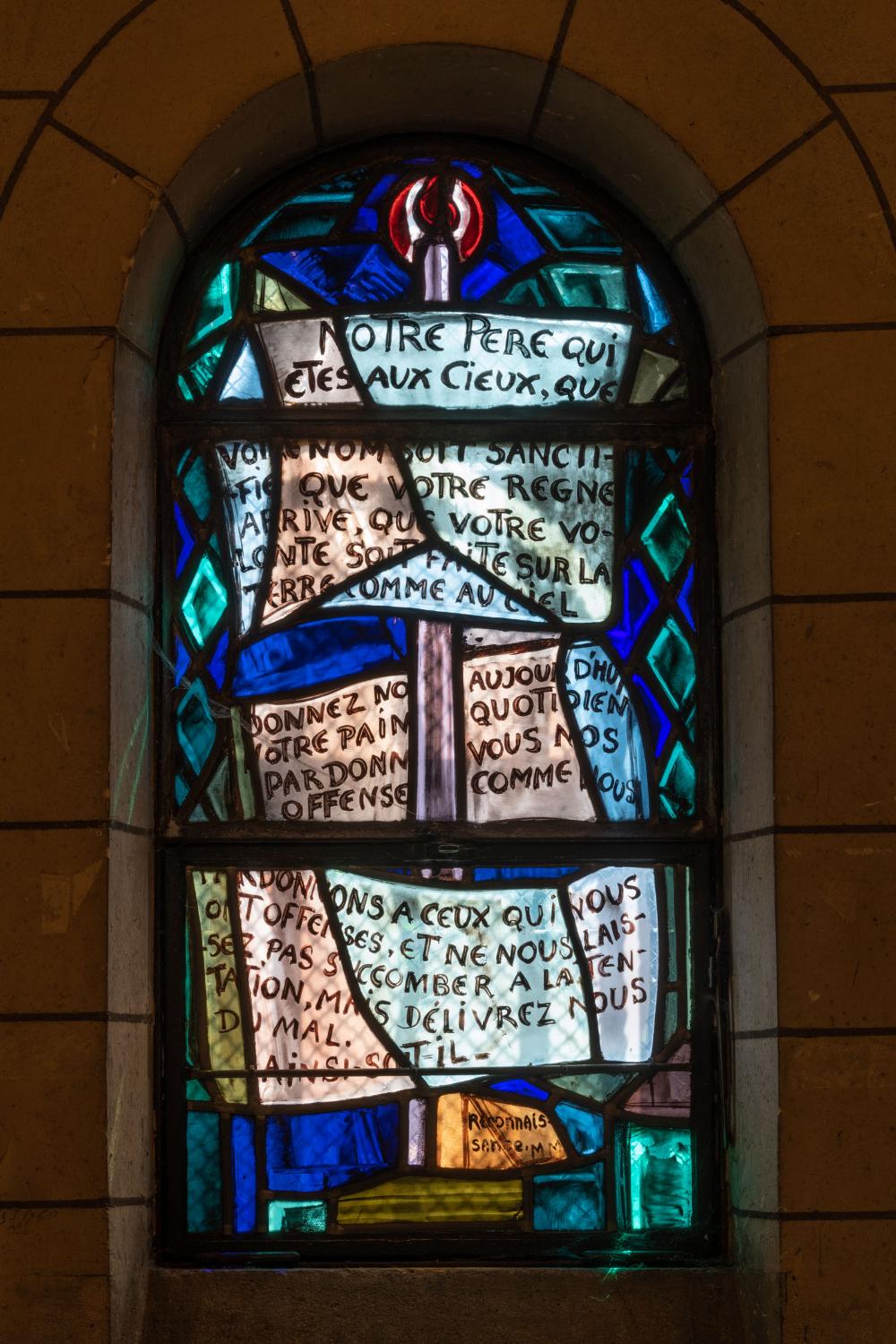 Dans la chapelle-baptistère, vue générale du vitrail de Valentine Reyre représentant le Notre-Père (1937). 