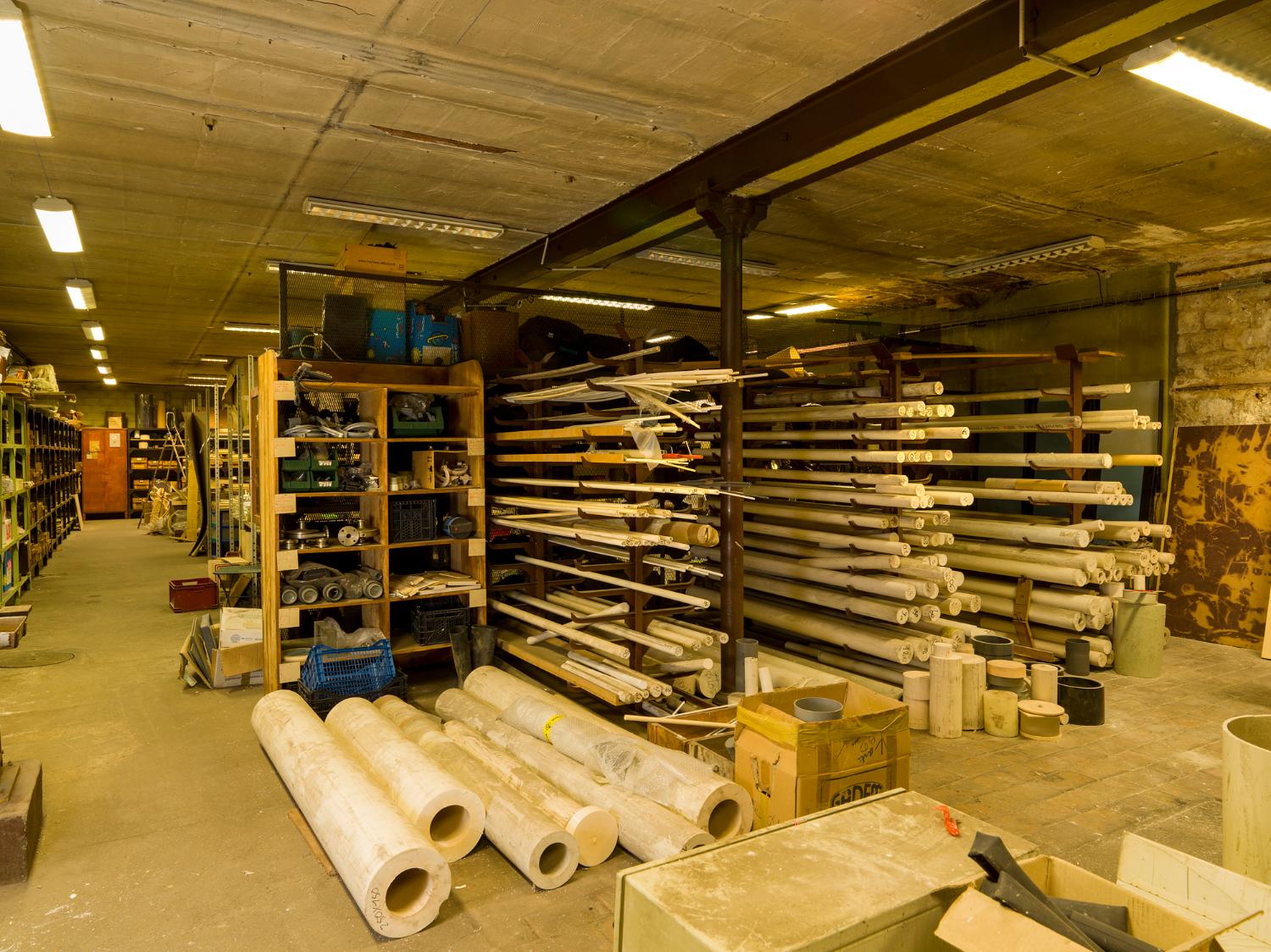 Stockage des matières premières pour usinage sur machines-outils, au sous-sol. À l’arrière, magasin d’accessoires et de pièces détachées.