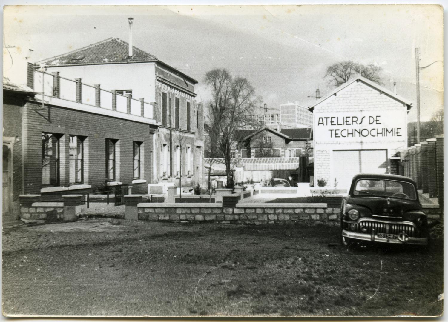 Transformation de la façade des bureaux des Ateliers de Technochimie. À droite, le bâtiment abrite un garage au rez-de-chaussée et le réfectoire à l'étage. Tirage photographique noir et blanc, 9 x 12,5 cm, 25 décembre 1960, sans mention d'auteur (collection Ateliers de Technochimie).